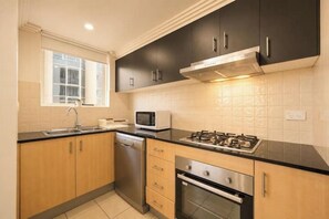 A kitchen with a stove, microwave, and dishwasher. - Boutique Property | Pool, Tennis & Jetty (Bundall)