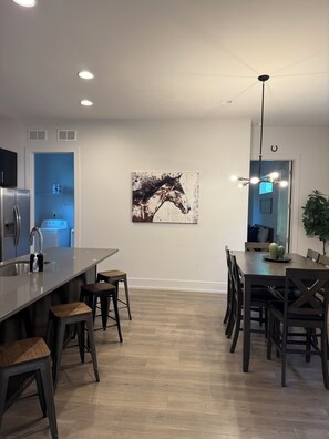 A modern kitchen with a central island, bar stools, and a dining area with a chandelier. - Spacious 4-bedroom house across from Pickleball Park near Uptown (Charlotte)