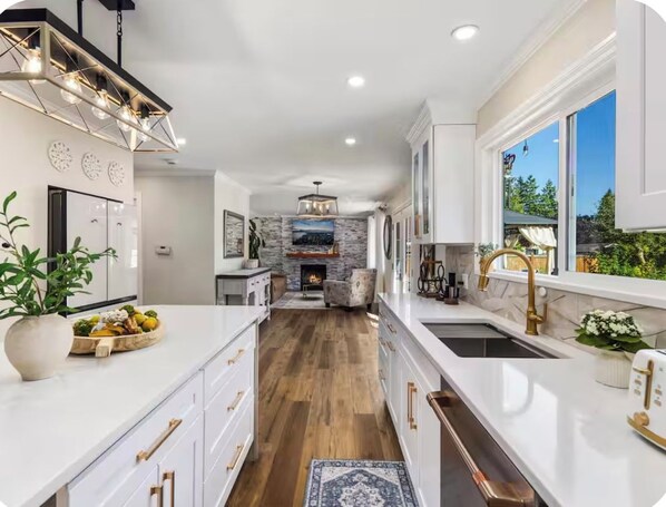 A modern kitchen with white cabinetry, a central island, and a stone fireplace.