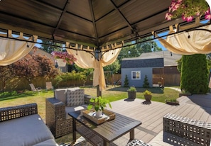 A covered patio with outdoor furniture, a table with a plant, and hanging flower baskets.