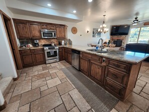 Una cocina con armarios de madera, electrodomésticos de acero inoxidable, encimera de granito y suelo de piedra.