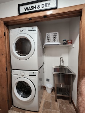 A laundry area with two stacked washing machines, a small sink, and a shelf with laundry supplies. - Black Diamond Lakeview Retreat, Ski In/Out + Hot Tub (Brian Head)