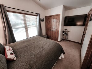 A bedroom with a bed, a TV mounted on the wall, a wooden door, and a window with blinds. - Black Diamond Lakeview Retreat, Ski In/Out + Hot Tub (Brian Head)