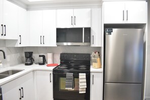 A modern kitchen with white cabinets, a stainless steel refrigerator, a black stove, and a microwave. - Cozy & Spacious 2 BR Basement| Home away from home | Sleeps 6 (Airdrie)