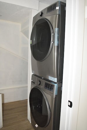 Eine übereinander gestellte Waschmaschine und Trockner in einem Raum mit Holzboden und weißen Wänden.