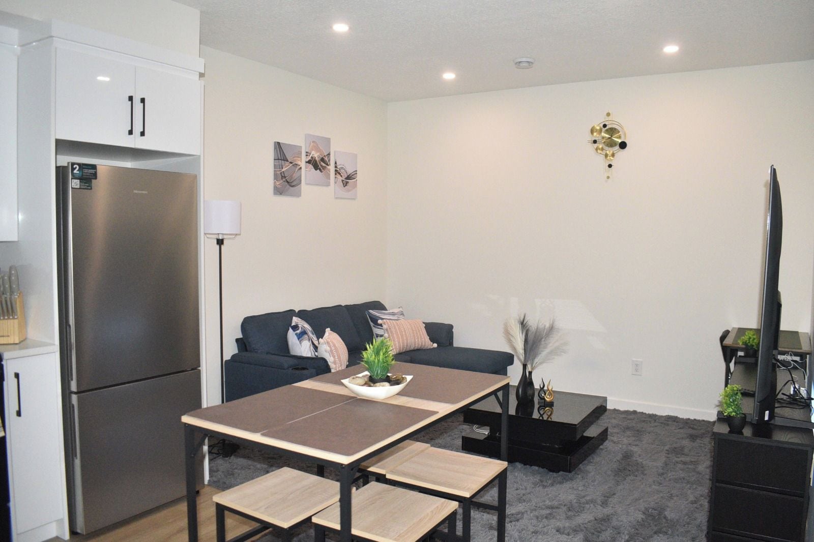 A compact living space with a kitchenette, a dining table, a sofa, and a flat-screen TV.