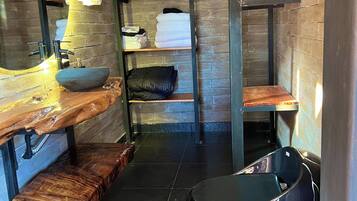 Un baño pequeño con un tocador de madera, un lavabo negro y un cubo de basura negro.