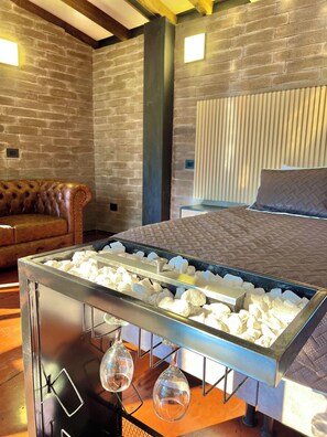 A room with a brick wall, a leather sofa, a bed with a quilted cover, and a glass-top coffee table with a metal frame. - Private Cabin to Enjoy Luxury and Comfort (Rionegro)