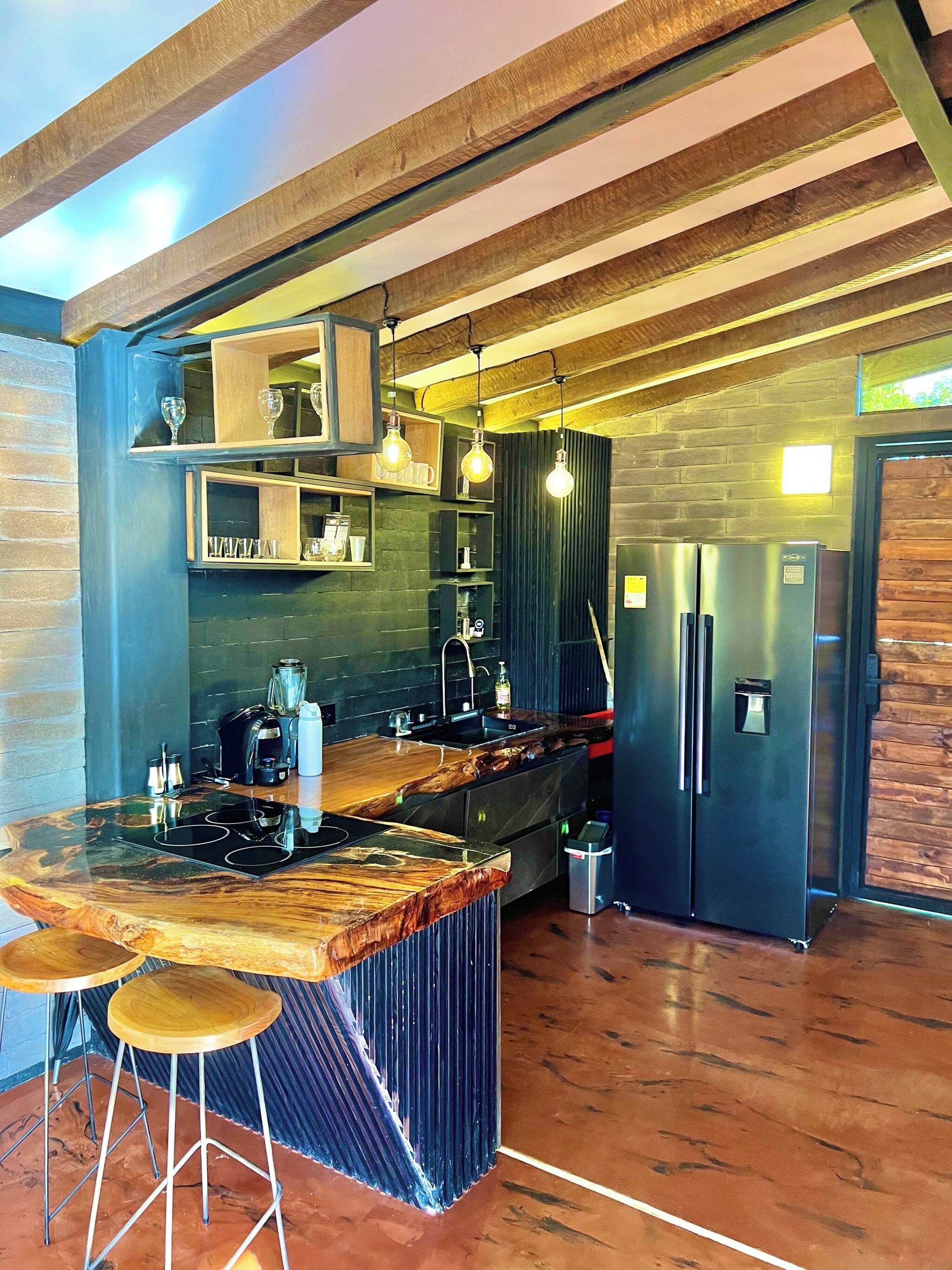 Cozinha moderna com ilha central, banquetas, geladeira e iluminação pendente.