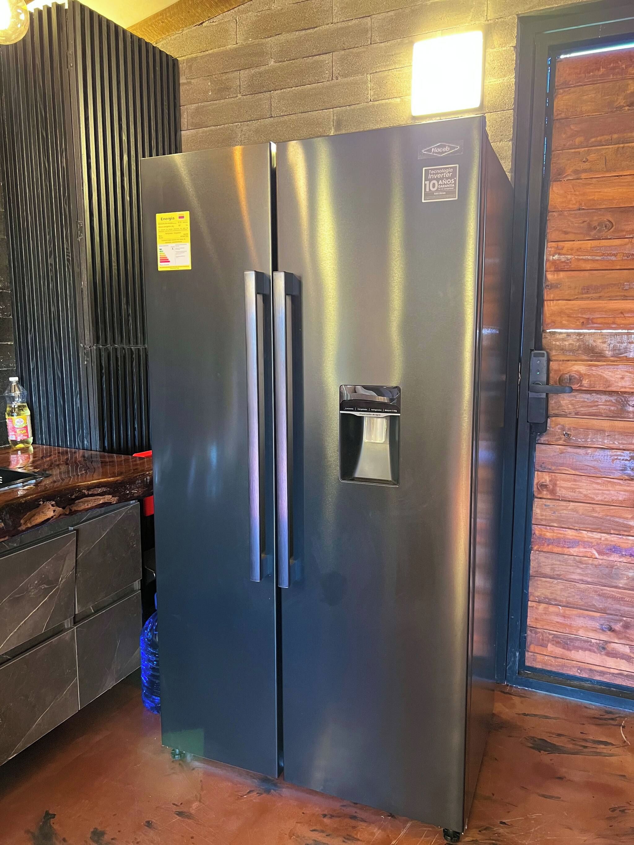 Een koelkast van roestvrij staal met een digitaal slot en bedieningspaneel, in een keuken met een houten wand en een betegelde vloer.