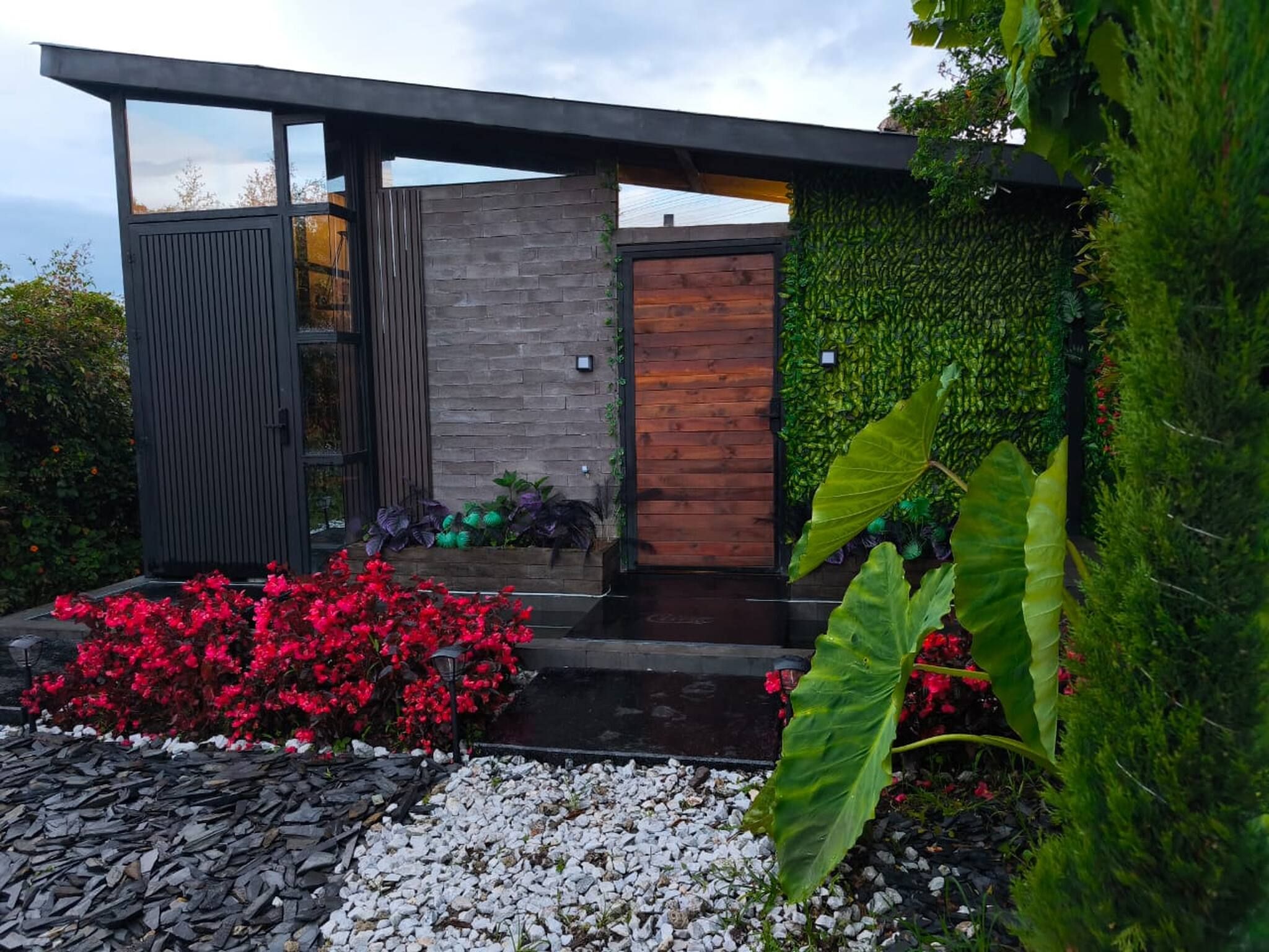 A modern house with a wooden door, a stone wall, and a green wall with plants.