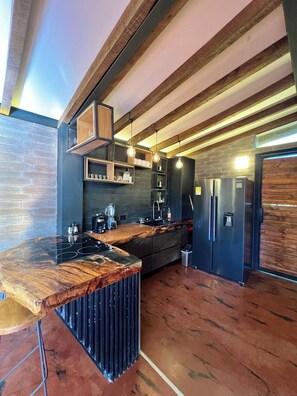 Une cuisine moderne dotée d’un îlot central en bois, d’étagères intégrées et d’un réfrigérateur noir.