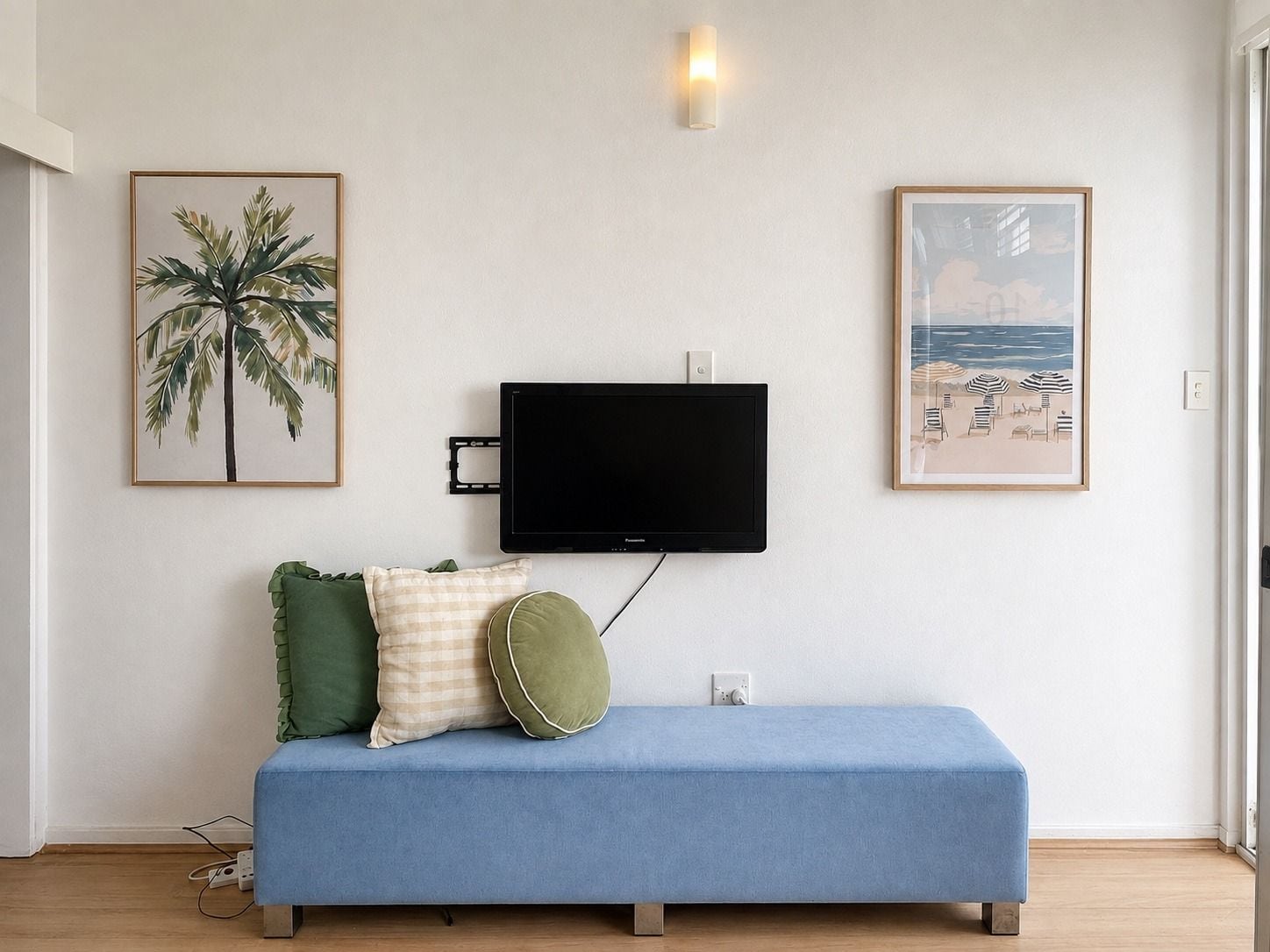 Quarto com sofá azul, televisão de tela plana na parede e duas imagens emolduradas.