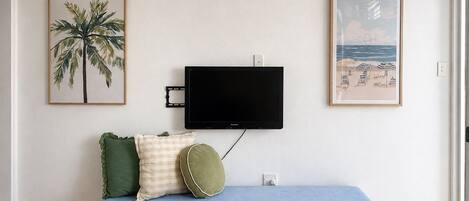 A room with a blue sofa, a flat-screen TV mounted on the wall, and two framed pictures.