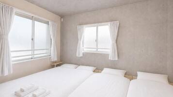 Ein Hotelzimmer mit zwei Betten, einem kleinen Nachttisch und zwei mit Vorhängen versehenen Fenstern.