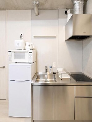 Cocina moderna con electrodomésticos de acero inoxidable, incluyendo un microondas y un refrigerador, y un lavamanos con grifo.