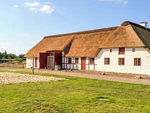 A traditional thatched-roof building with a white exterior and red accents, situated in a grassy area with a clear sky. - 6 Person Holiday Home in Blavand (Blavand)