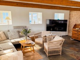Ein Wohnzimmer mit einer Couch, Korbstühlen, einem Couchtisch und einem Fernseher.