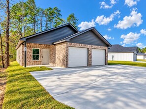A two-story residential building with a brick facade, a garage with two white doors, and a well-maintained lawn. - Cozy 2-bedroom house in perfect Lufkin with AC for relaxing stays (Lufkin)