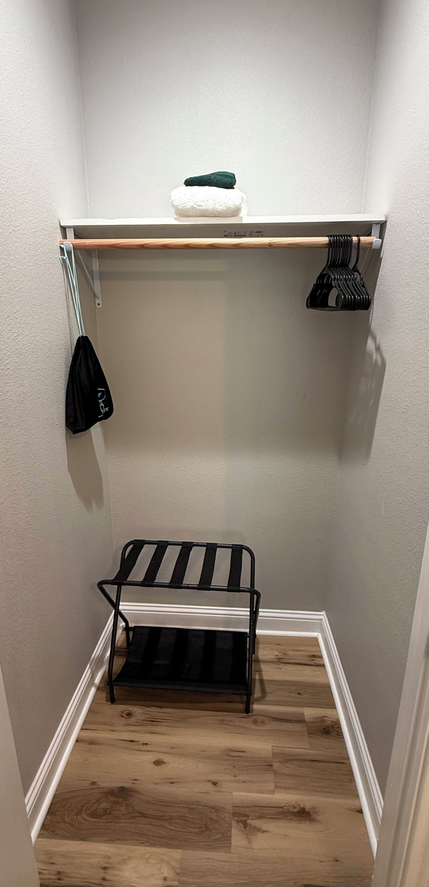 Un petit placard avec une étagère en bois, un cintre noir et un sac noir.