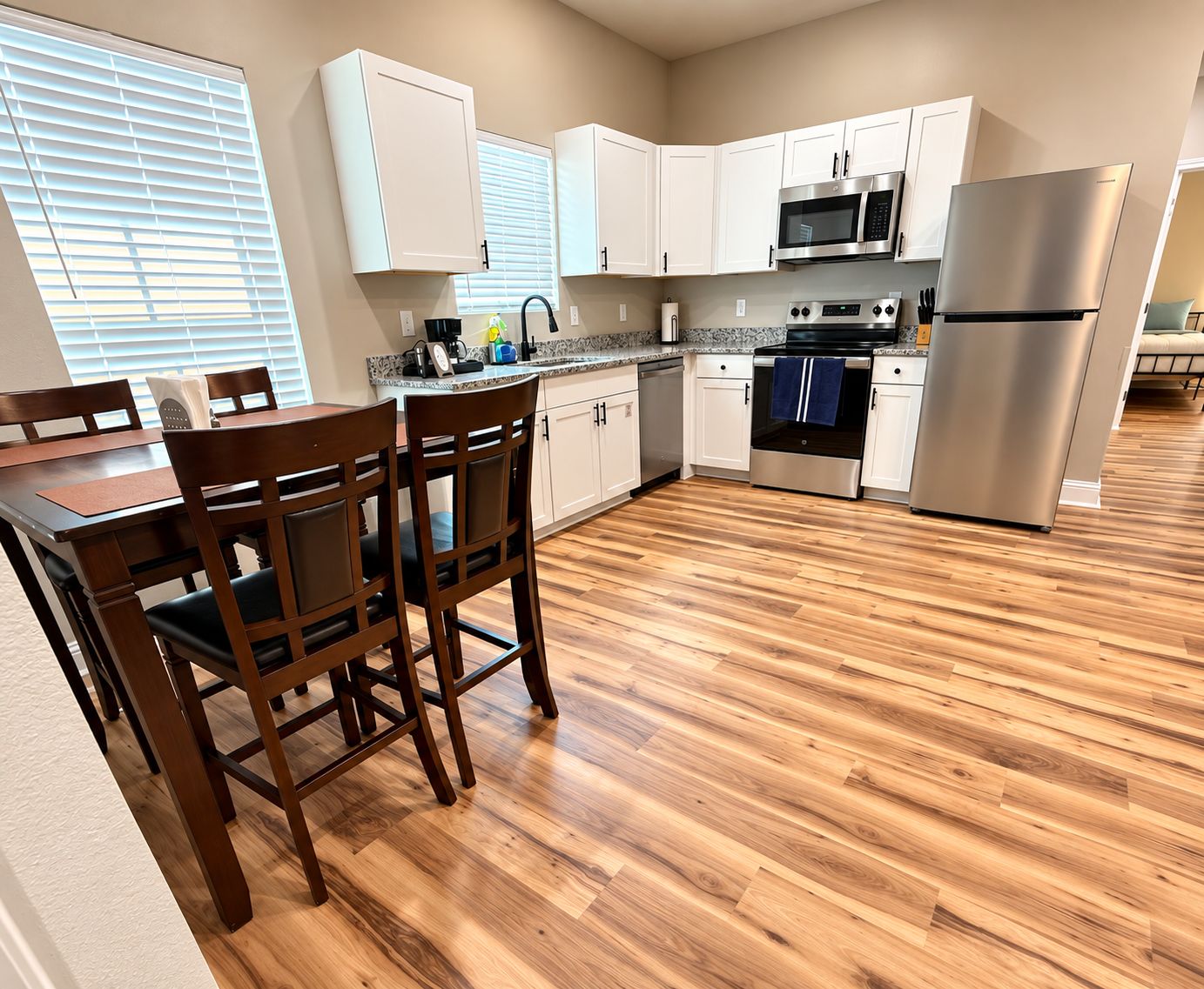A modern kitchen with white cabinets, stainless steel appliances, and a wooden dining table with chairs.