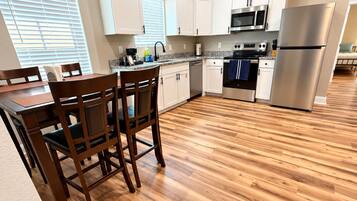 A modern kitchen with white cabinets, stainless steel appliances, and a wooden dining table with chairs.