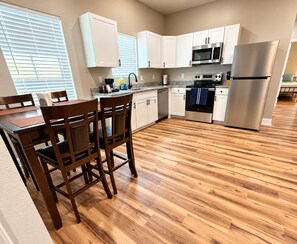 A modern kitchen with white cabinets, stainless steel appliances, and a wooden dining table with chairs. - Cozy 2-bedroom house in perfect Lufkin with AC for relaxing stays (Lufkin)