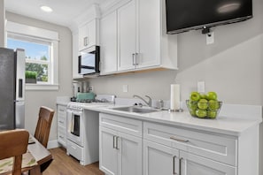A modern kitchen with white cabinetry, a gas stove, a microwave, and a flat-screen TV mounted above the counter. - Boise 1BR w/ Patio Near BSU, Downtown & Airport (Boise)
