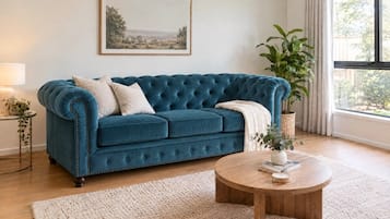 A living room with a blue sofa, a round wooden coffee table, and a large window with curtains.