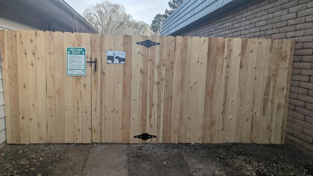 Una cerca de madera con un cartel de normas del parque canino y la silueta de un perro negro.