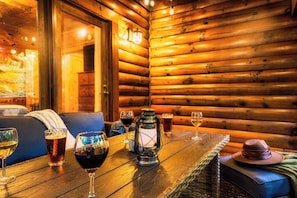 Een knus cabin interieur met een houten wand, een eettafel met wijnglazen en een blauwe bank.