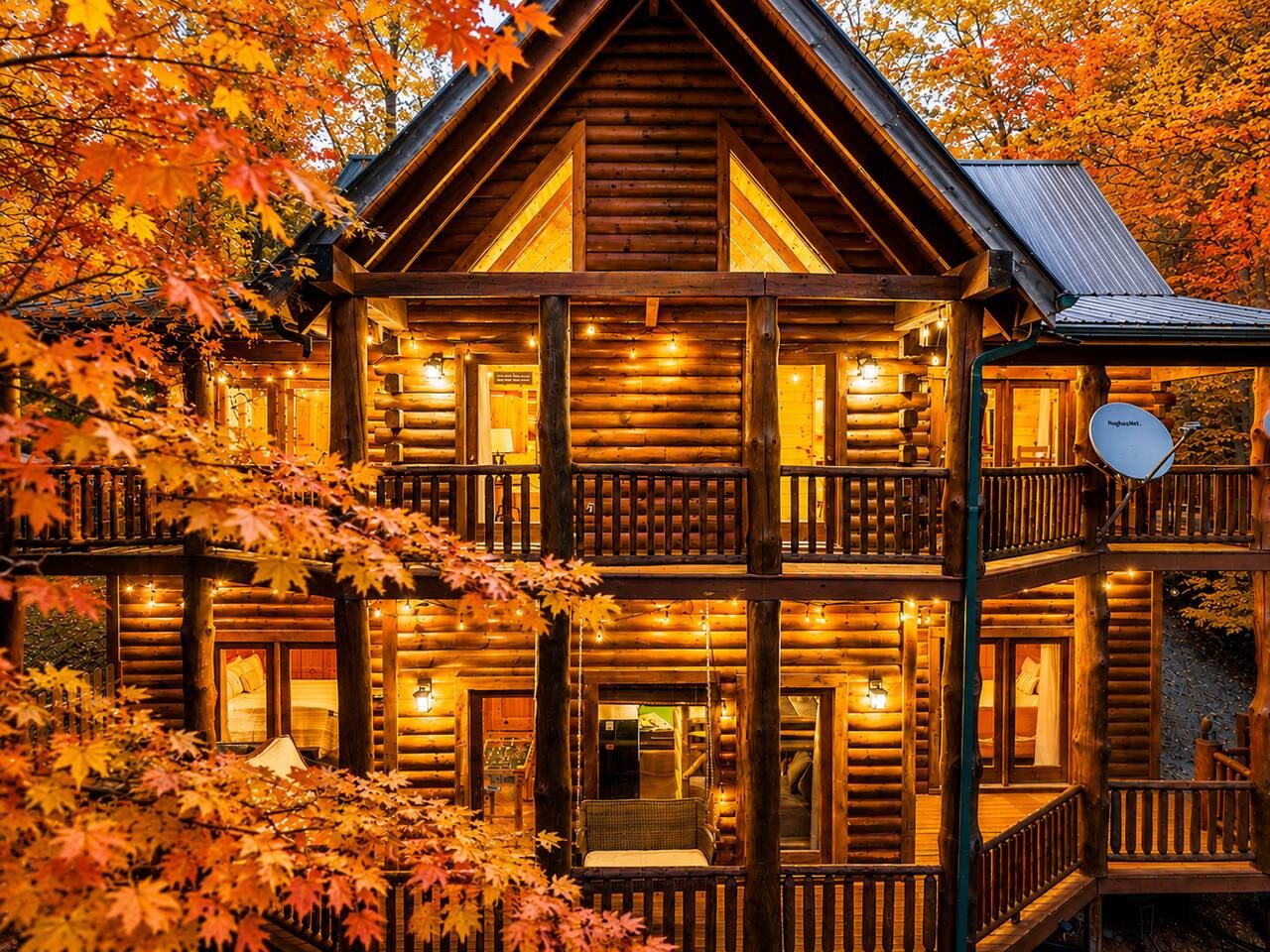 A multi-story log cabin with a balcony on the second floor, surrounded by autumn foliage.