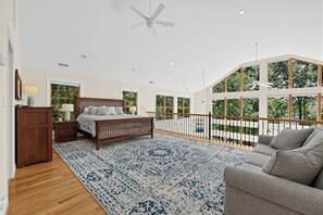 Een slaapkamer met een groot bed, een houten nachtkastje, een dressoir, een kamerkleed met dessin en een balkon met een hekwerk.