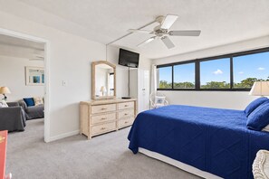 Ein Schlafzimmer mit Bett, Kommode, Fernseher, Deckenventilator und einem Fenster mit Blick.