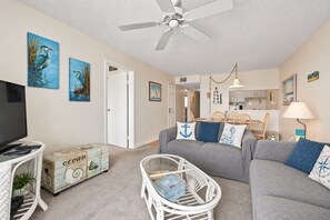 Ein Wohnzimmer mit grauem Sofa, Fernseher, weißem Tisch und Deckenventilator.