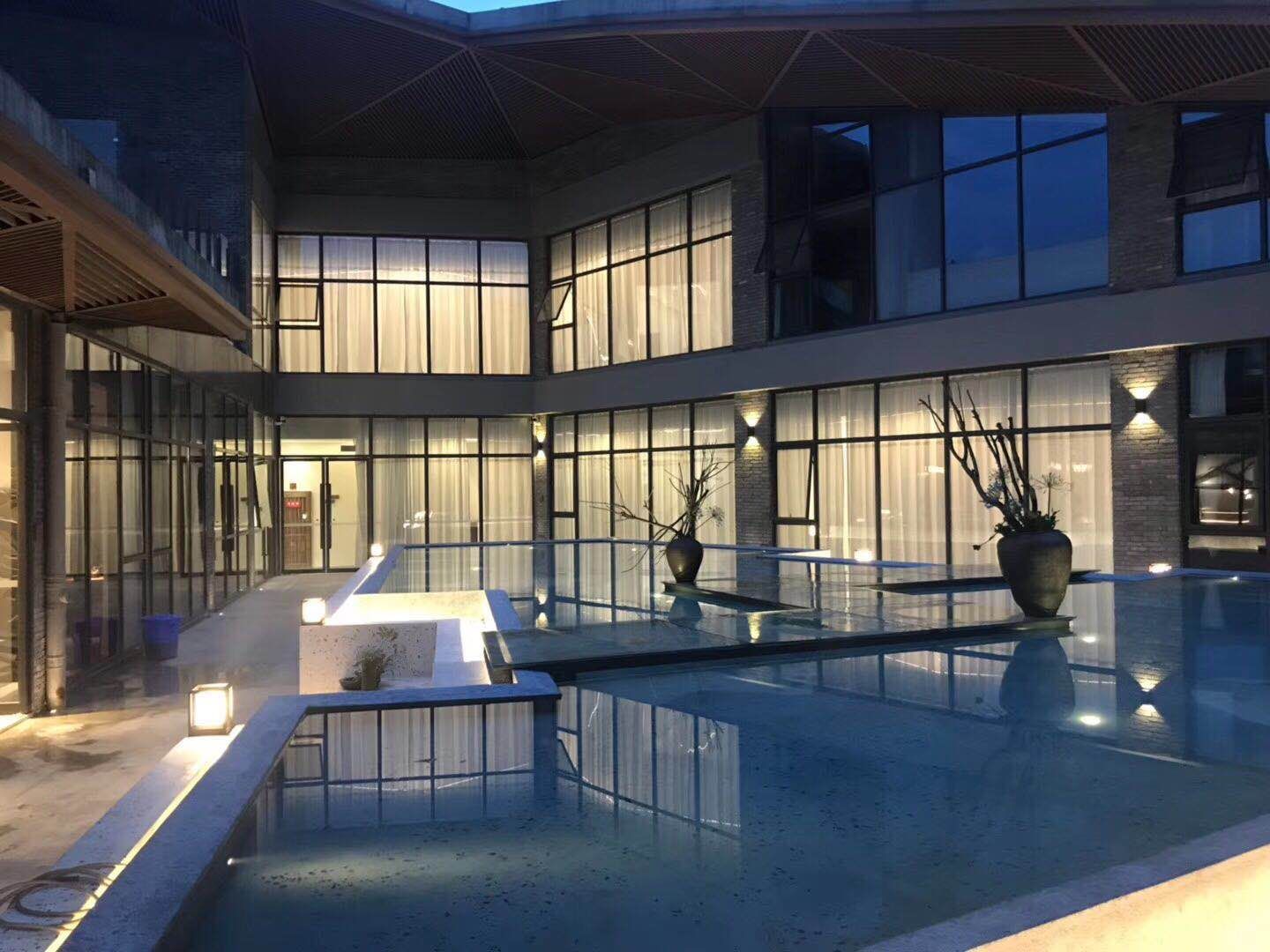 Edificio moderno con piscina en patio, ventanas amplias e iluminación exterior.