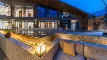 Un edificio moderno con un amplio espacio exterior, una zona de estar con cojines y una fuente de agua.