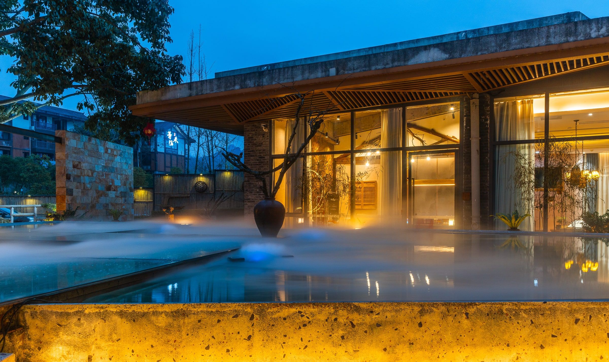 A modern building with a glass facade, a heated outdoor pool, and a stone wall.