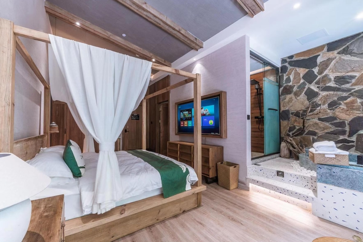 A bedroom with a four-poster bed, a television, and a stone wall.