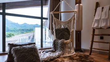 A room with a large window, a macramé hanging chair, a wooden ladder, and a fluffy rug.