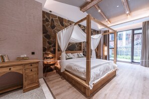 A bedroom with a four-poster bed, a wooden desk, a stone wall, and a large window.