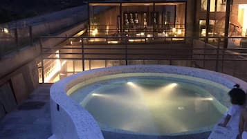 A hot tub with a child nearby, surrounded by a modern building with large windows and a balcony.