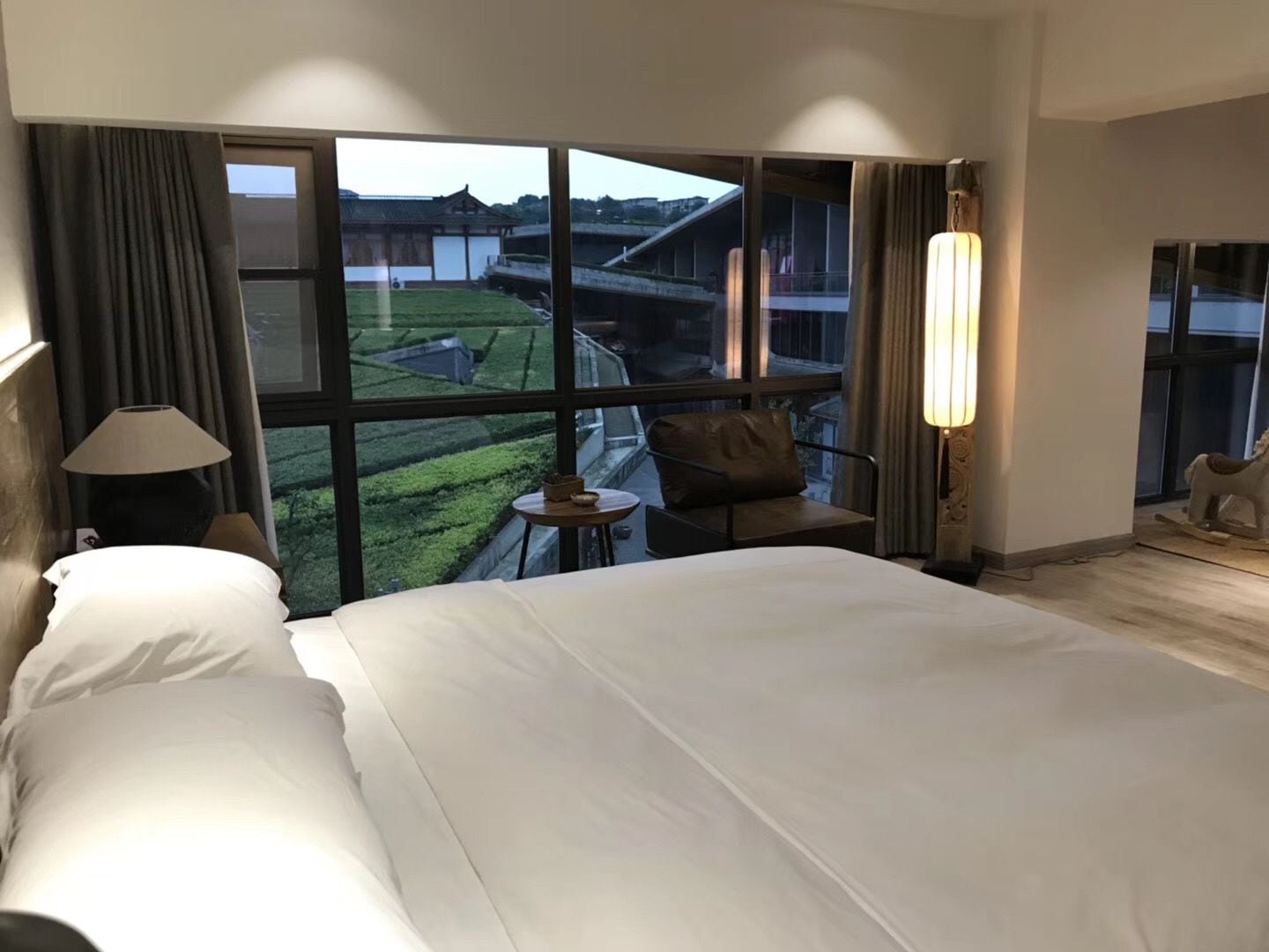 A hotel room with a large bed, a small table, a chair, and a view of the outside.