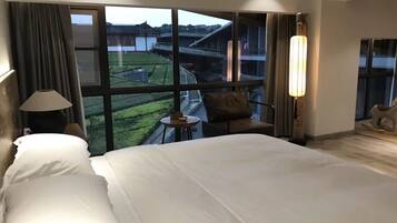 A hotel room with a large bed, a small table, a chair, and a view of the outside.