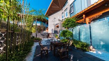 A courtyard with a table and chairs, surrounded by bamboo and a brick wall.