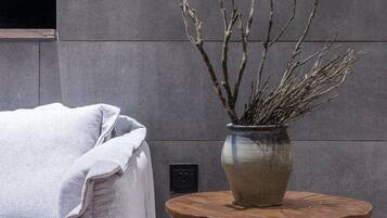 Una habitación moderna con un sofá gris, una mesa redonda de madera con un jarrón de ramas y una pared gris.