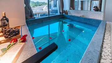 A swimming pool with a clear blue water, a book, a bottle, and some grapes on the side.