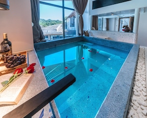 Una piscina con agua cristalina, un libro, una botella y algunas uvas al borde.