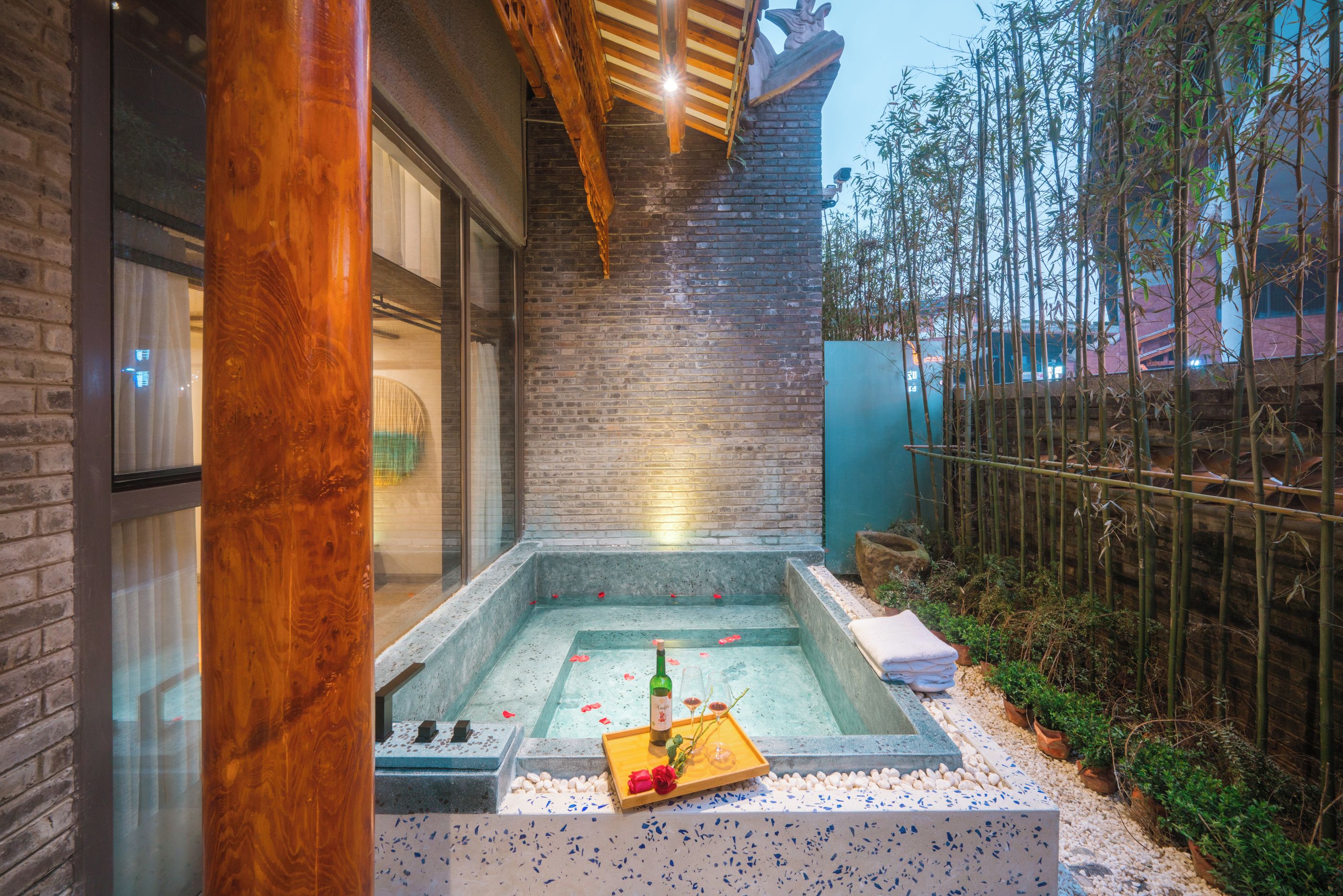 Un área de spa con un jacuzzi, rodeado por un muro de ladrillo y plantas de bambú.