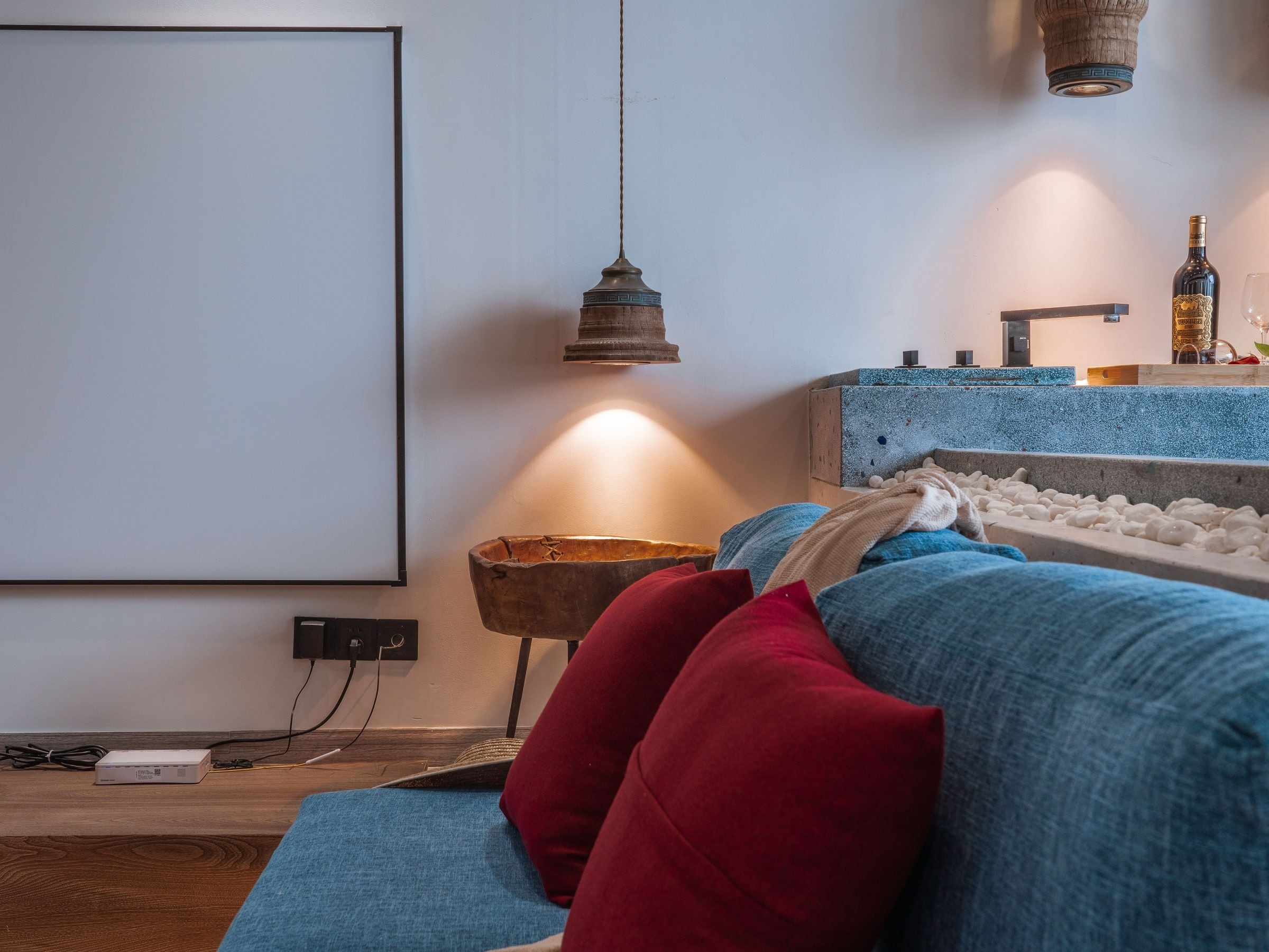 Una sala de estar moderna con un sofá azul, cojines rojos, un cuenco de madera y una lámpara colgante.